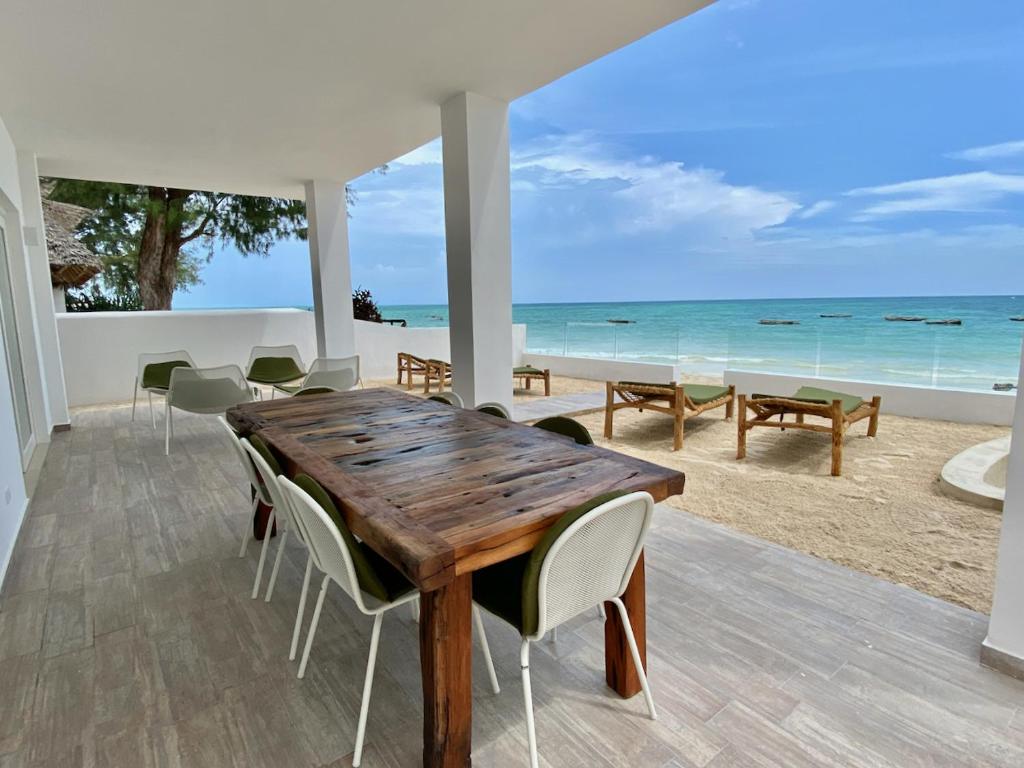 Ocean Blue Apartment with Panoramic Pool ZanzibarHouses في كيوينجوا: غرفة طعام مع طاولة خشبية والشاطئ