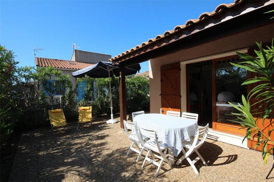 une table avec des chaises et un parasol sur une terrasse dans l'établissement Belle villa d'angle, cuisine séjour climatisé, 5 couchages, belle terrasse ombragée, parking dans résidence sécurisée piscine commune à 400m de la mer LRJP23, à Portiragnes