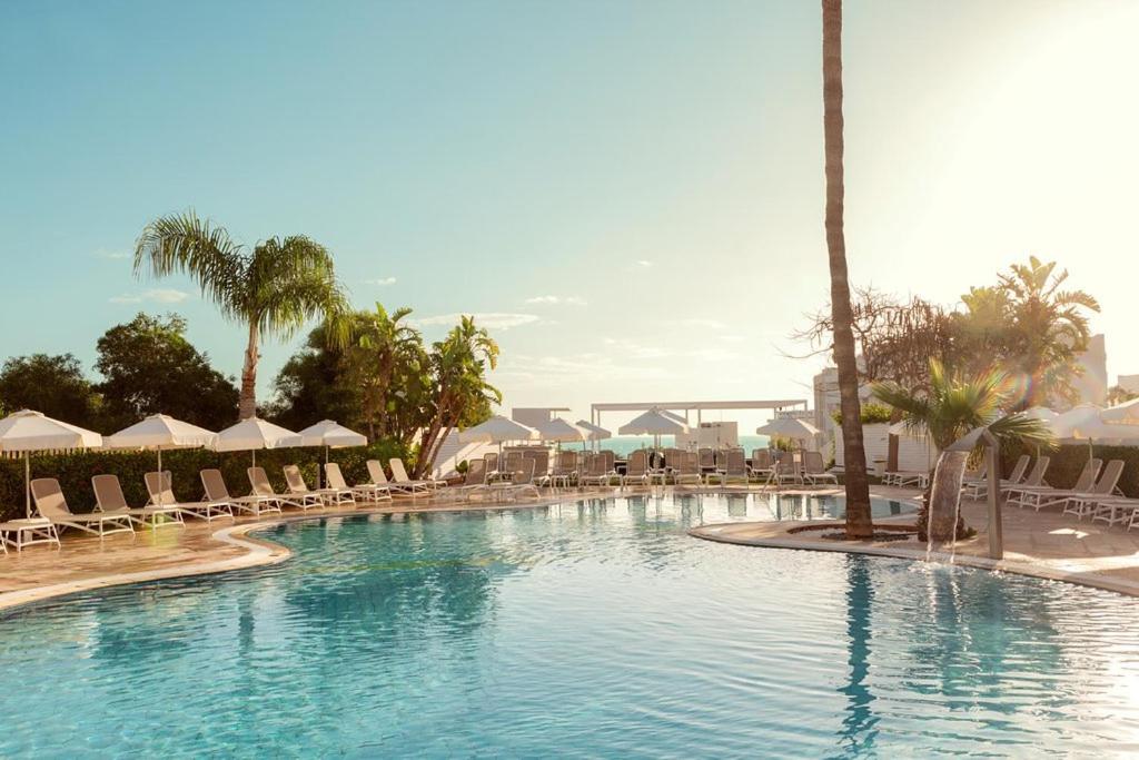 une grande piscine avec des chaises et des palmiers dans l'établissement Lantiana Gardens ApartHotel, à Protaras