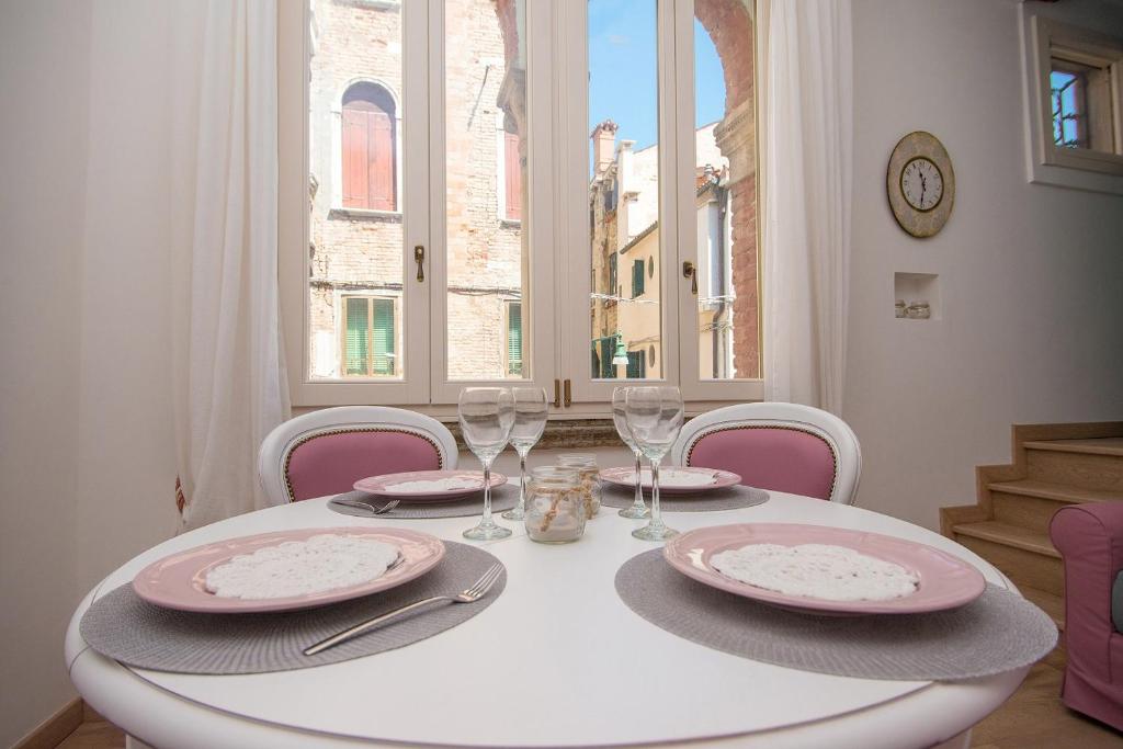 uma mesa branca com pratos cor-de-rosa e copos de vinho em Grimaldi Apartments Ca Del Moro em Veneza