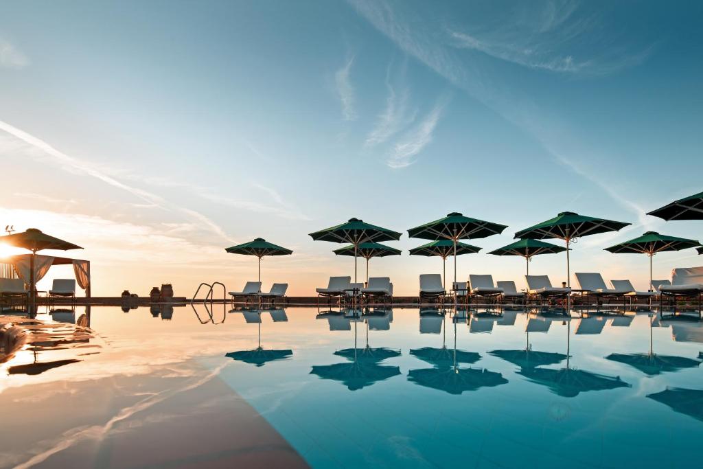 a pool with umbrellas and chairs and the sunset at Mitsis Lindos Memories Resort & Spa in Lindos