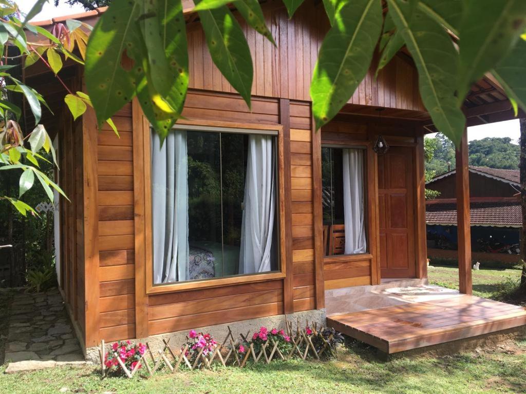 a wooden house with a porch and windows at Pedacinho de Chão Chalés in Visconde De Maua