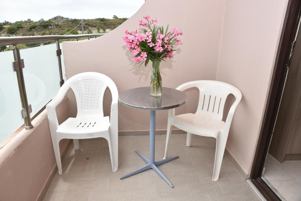 two chairs and a table with a vase of flowers on a balcony at Rose Hotel Faliraki in Faliraki