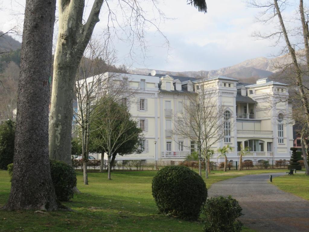 un grand bâtiment blanc avec des arbres devant lui dans l'établissement Le Balcon du Parc, entre Lourdes et Gavarnie, à Argelès-Gazost