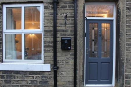 a brick building with a blue door and two windows at Haworth Bronte House Cottage in Haworth