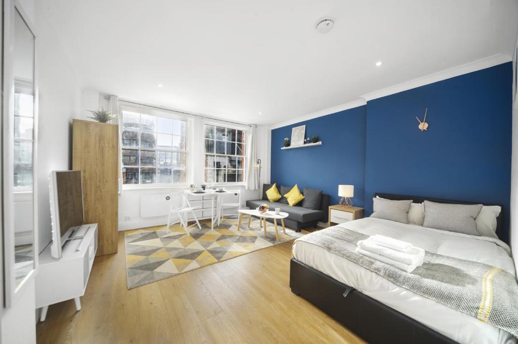 een slaapkamer met blauwe muren en een bed en een bank bij Studio Apartment by Homely Stays in Londen