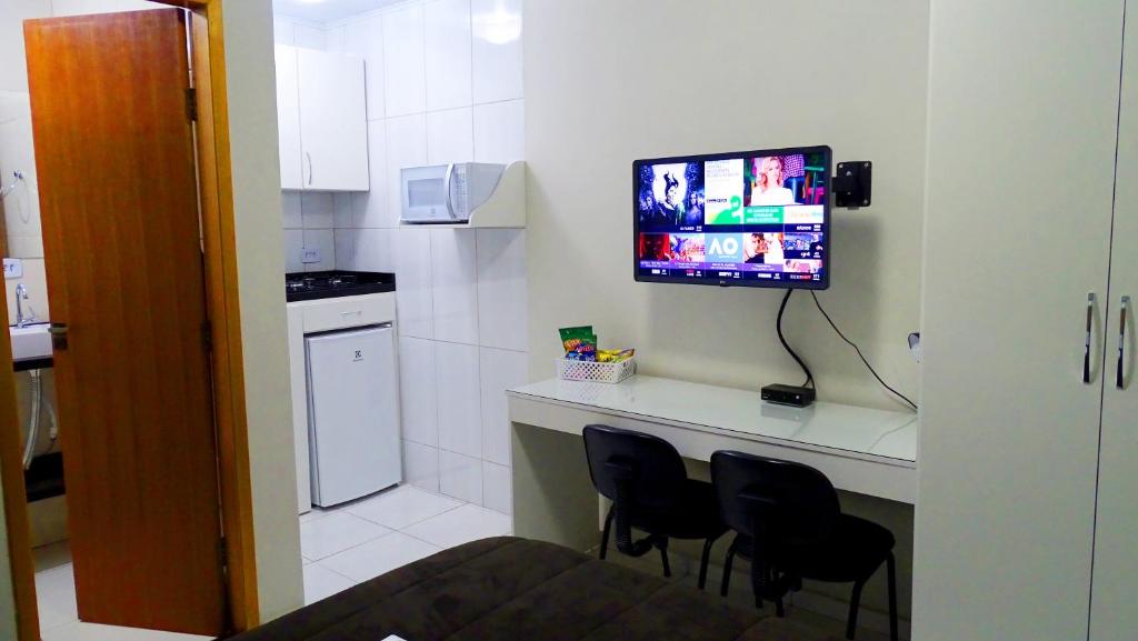 a kitchen with a counter with chairs and a tv on the wall at Flat 02 in Jaguariaíva