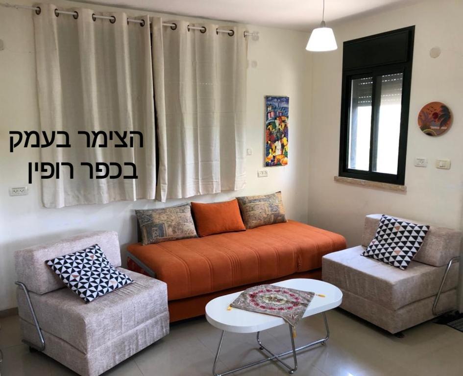 a living room with an orange couch and two chairs at צימר בעמק in Kefar Ruppin