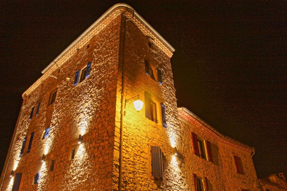 um edifício de tijolos alto com luzes acesas à noite em Gîtes La Tour le Mas de Crieulon em Saint-Jean-de-Crieulon