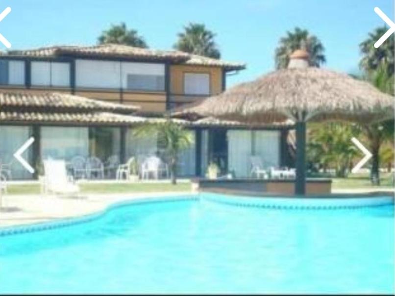 una piscina con sombrilla de paja y un edificio en Apart Hotel em Búzios, en Búzios