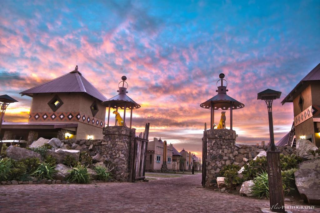 a building with a gate with a sunset in the background at Emoya Basotho Lodge in Bloemfontein