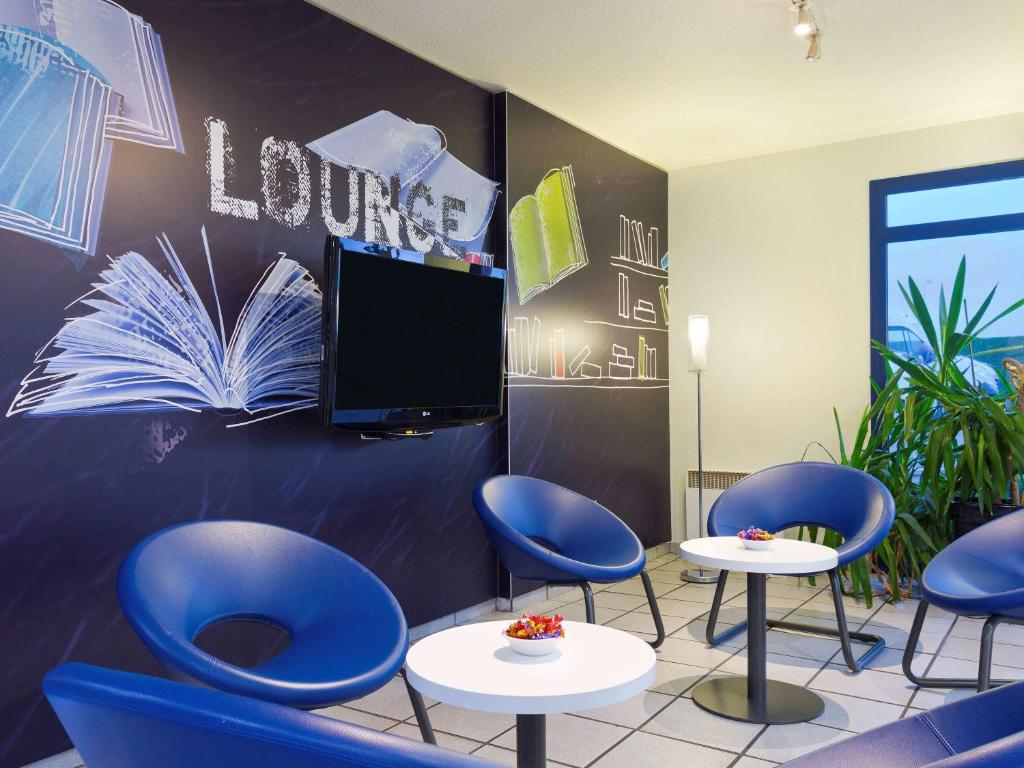 uma sala de espera com cadeiras azuis e uma televisão de ecrã plano em ibis budget Chilly-Mazarin Les Champarts em Chilly-Mazarin