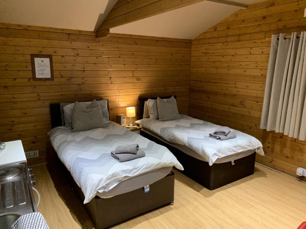 two beds in a room with wooden walls at Southernwood - Garden Lodge 2 in Didcot