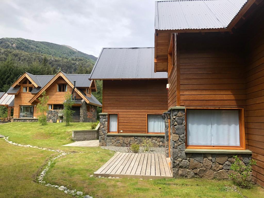 un grupo de casas de madera con montañas en el fondo en La lucinda en Villa La Angostura