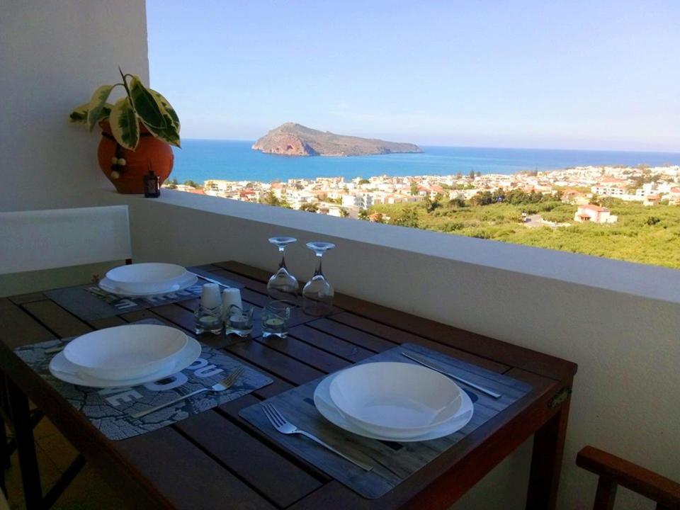 stolik z talerzami i kieliszkami oraz widok na ocean w obiekcie Thea Apartment w mieście Agia Marina Nea Kydonias