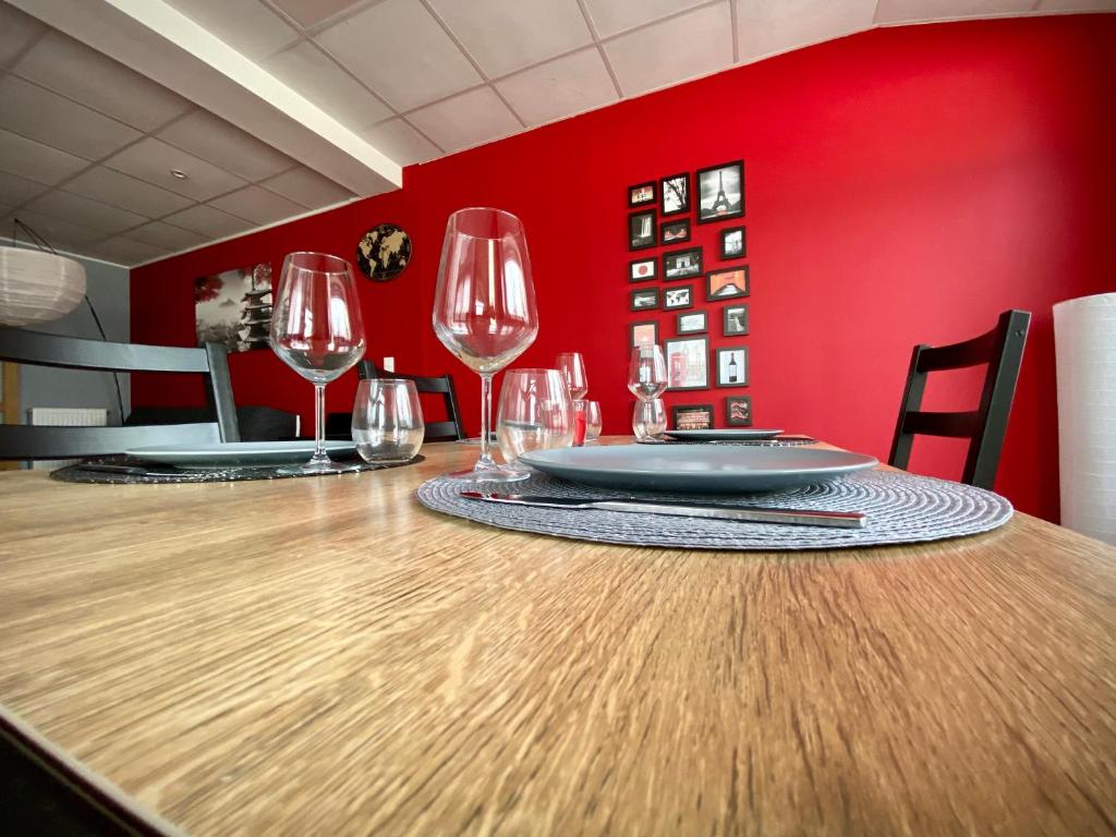 a table with wine glasses on a red wall at Logements équipés à Onnaing avec espace Balneo en OPTION proche Toyota, autoroute et Valenciennes in Onnaing
