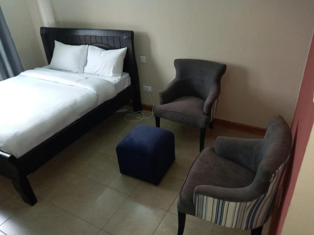 Nairobi west suite في نيروبي: غرفة نوم مع سرير وكرسيين والعثمانية