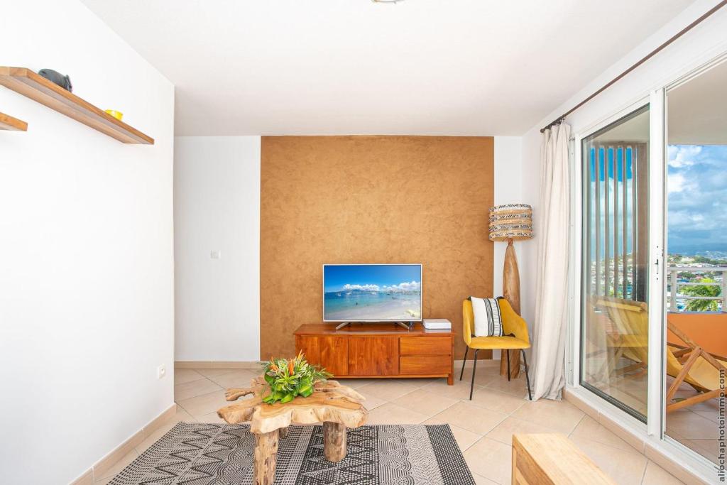 Appart Hotel Martinique - Mellow Yellow في Ducos: غرفة معيشة مع تلفزيون بشاشة مسطحة على جدار