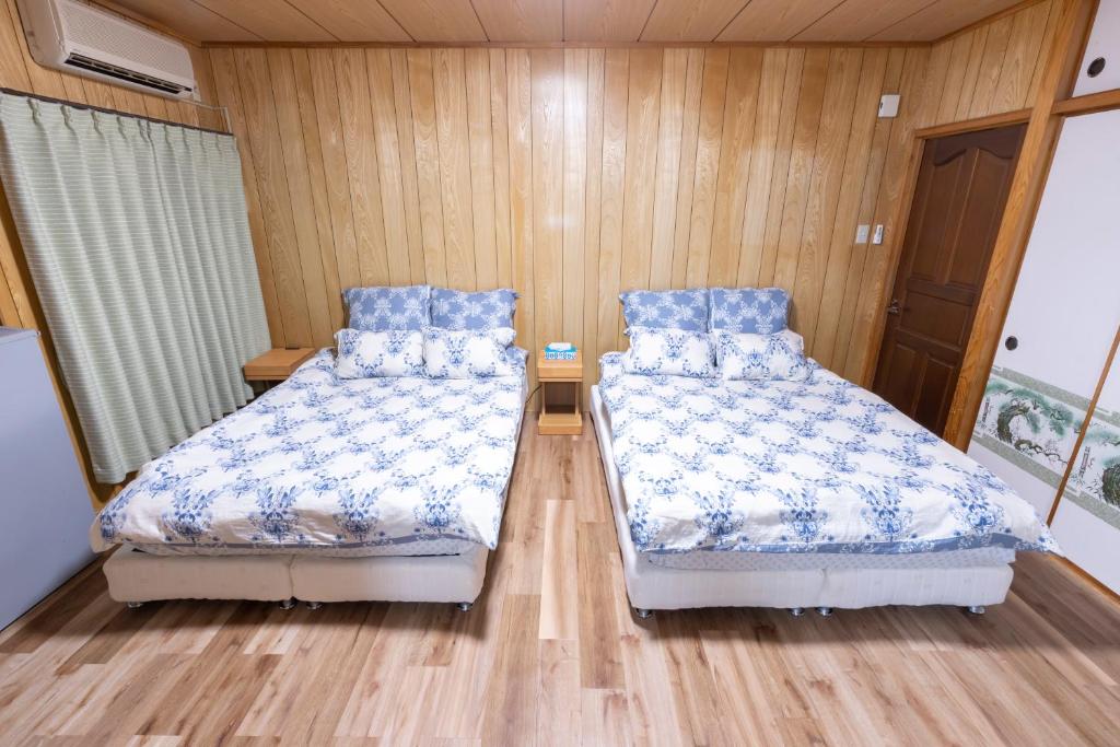two beds in a room with wooden walls and wooden floors at kamekamehouse in Tokashiki