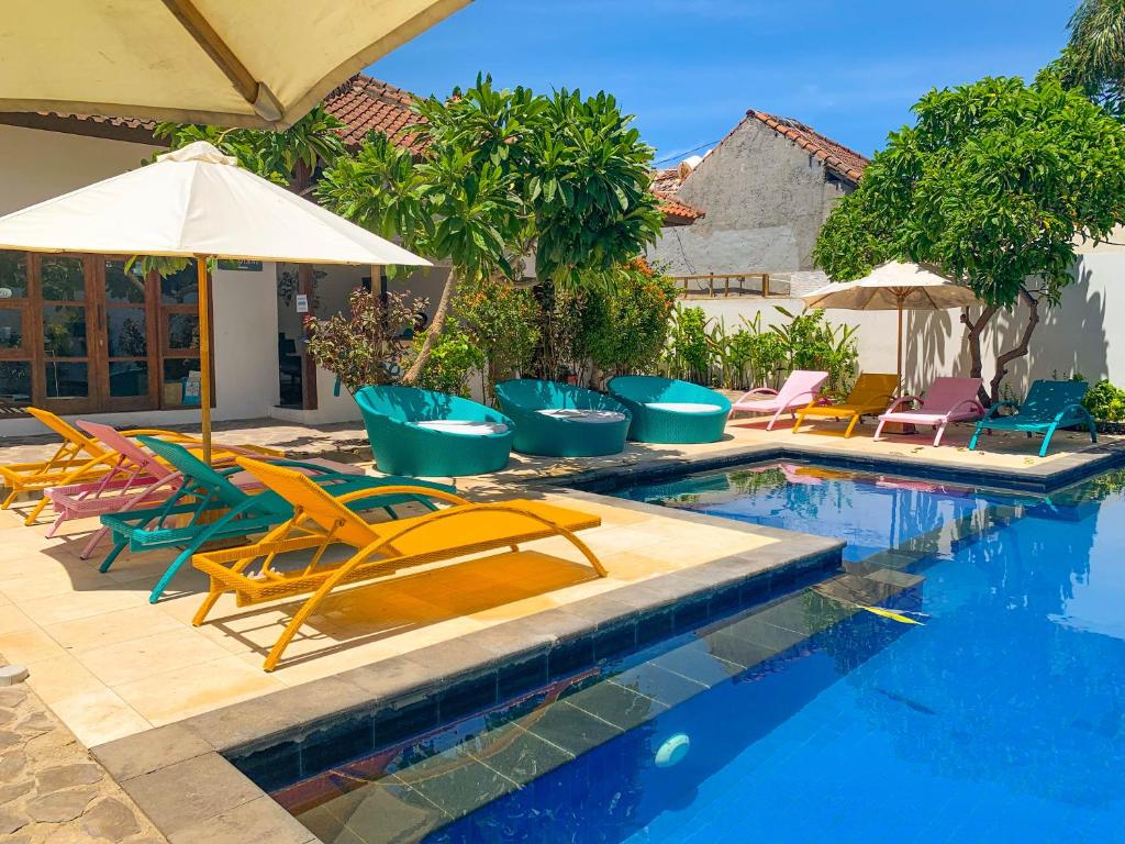 a swimming pool with lounge chairs and an umbrella at Tír na nÓg Beachfront Resort in Gili Trawangan