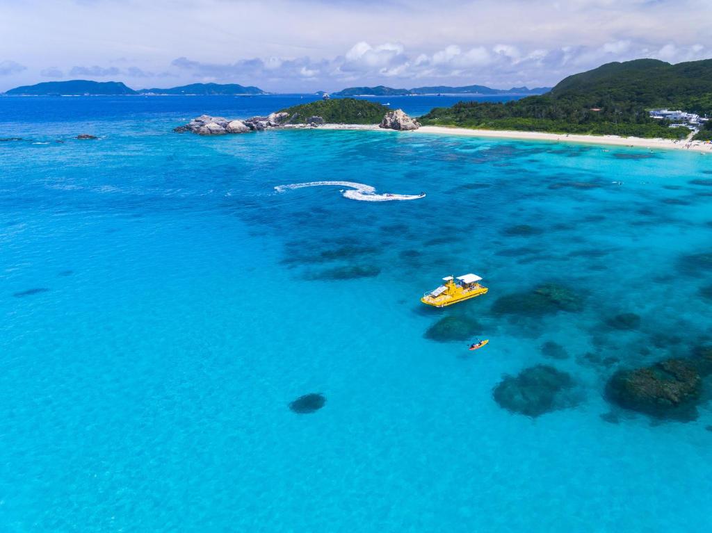 un barco amarillo en el agua junto a una playa en kamekamehouse, en Tokashiki