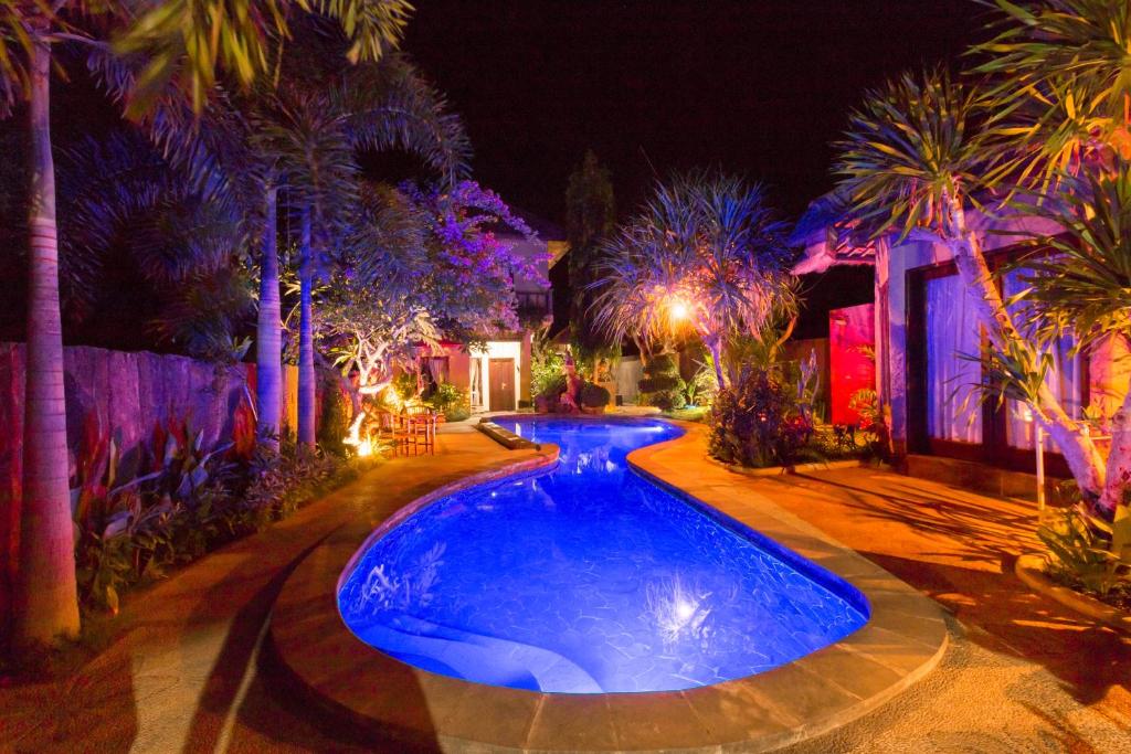 a swimming pool in a yard with palm trees at night at Pondok Mimpi Tulamben in Tulamben