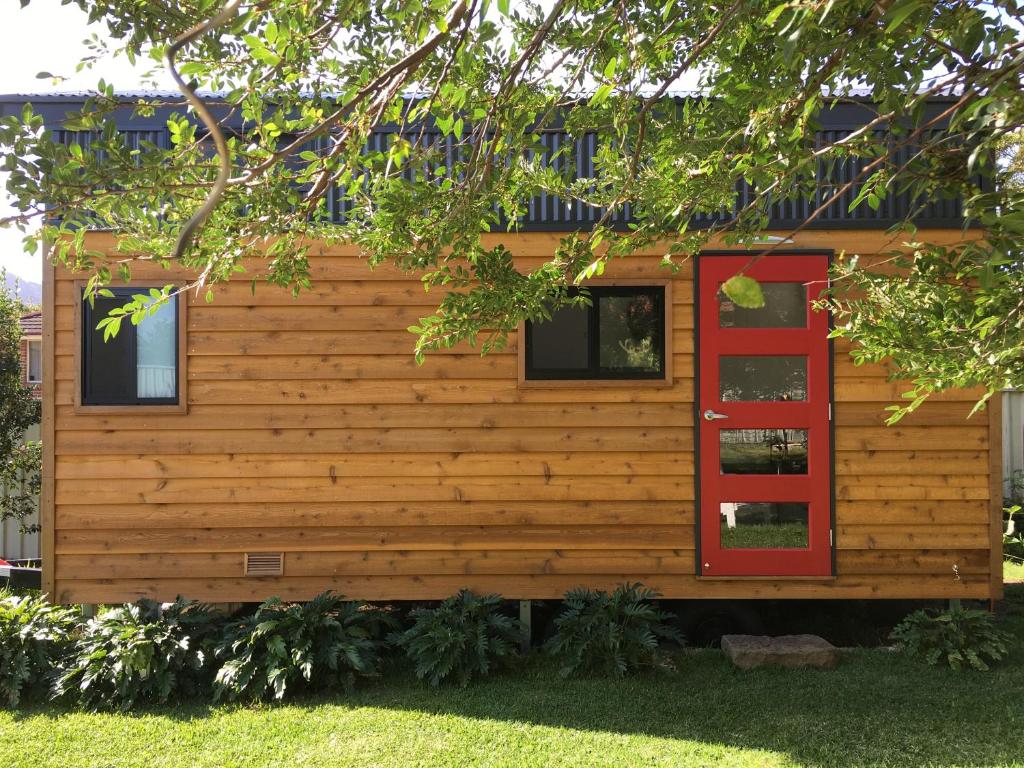 a log cabin with a red door and windows at Tiny House in Woonona