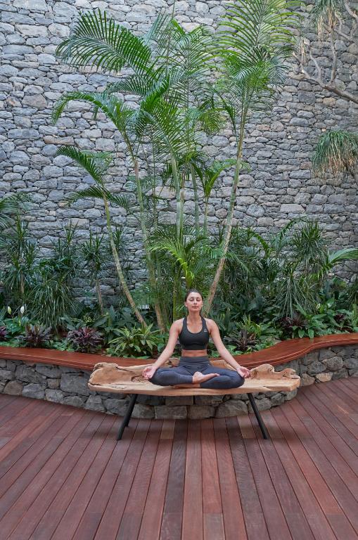 a woman is sitting in a yoga position on a bench at Les Suites at The Cliff Bay - PortoBay in Funchal