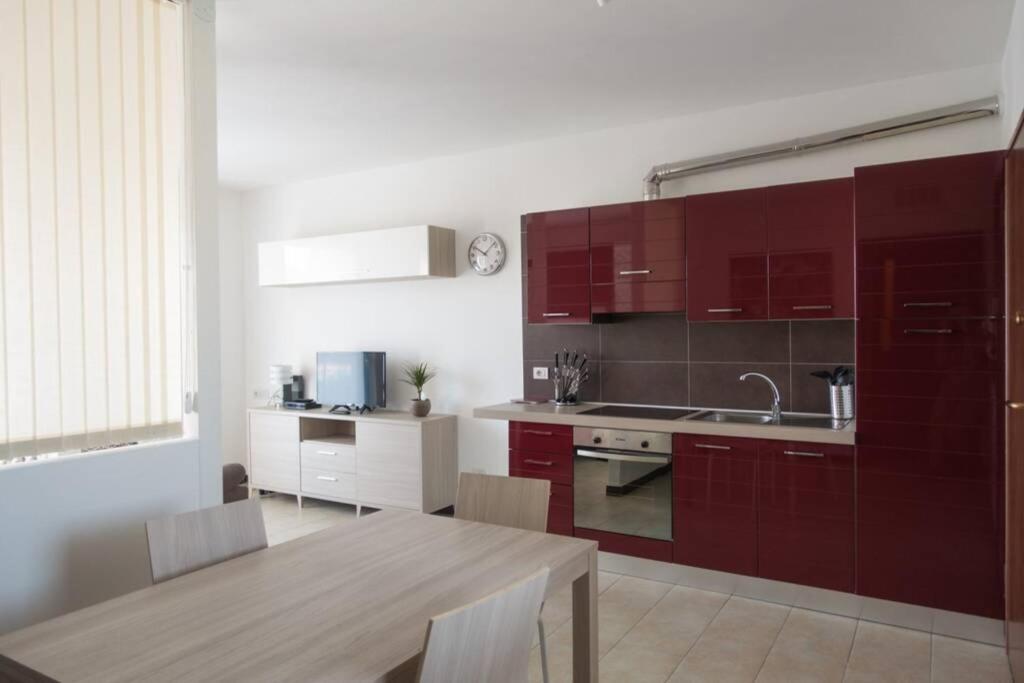 kuchnia z czerwonymi szafkami i drewnianym stołem oraz tableablish w obiekcie Apartment Victoria, cozy studio flat near Leonardo Academy w mieście Sesto Calende