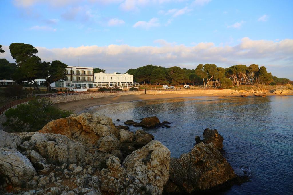 a beach with a building and rocks in the water at Hostal Empúries in L'Escala