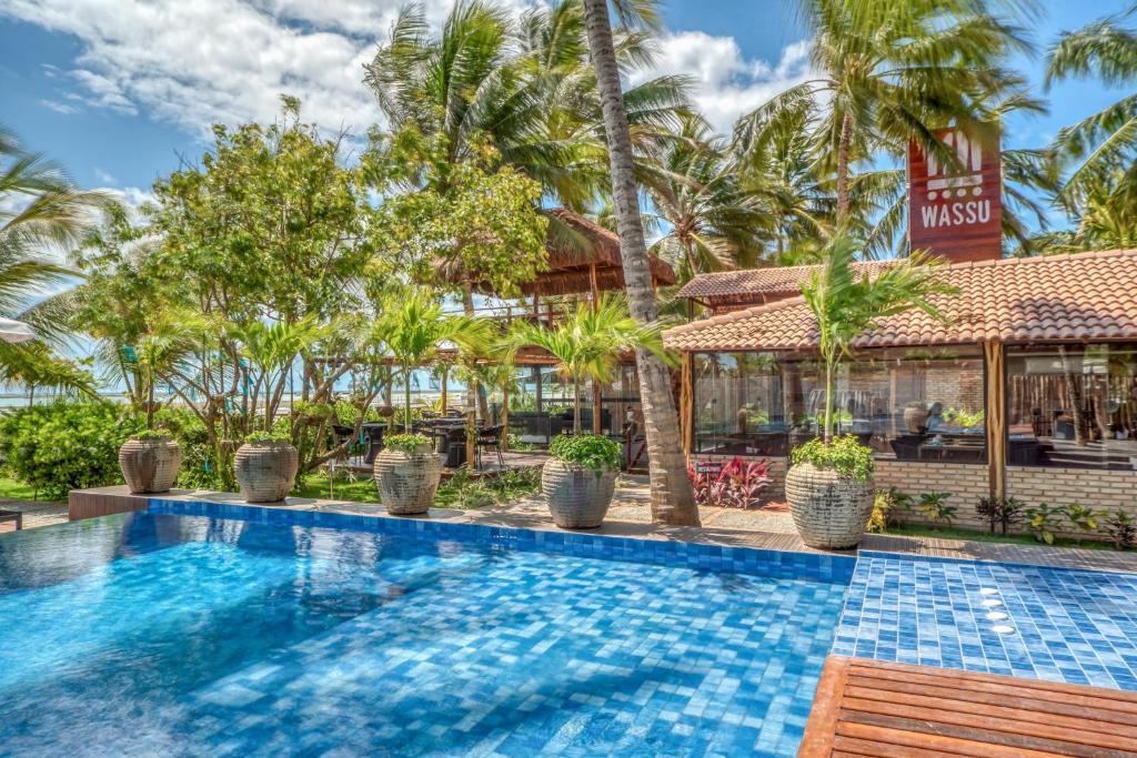 a swimming pool in front of a resort with palm trees at Wassu Pousada in São Miguel dos Milagres