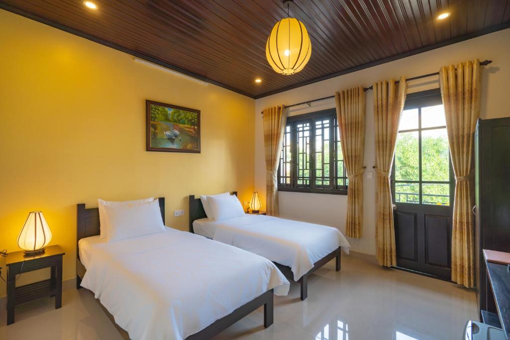 two beds in a room with yellow walls and windows at Old Lane Homestay in Hoi An