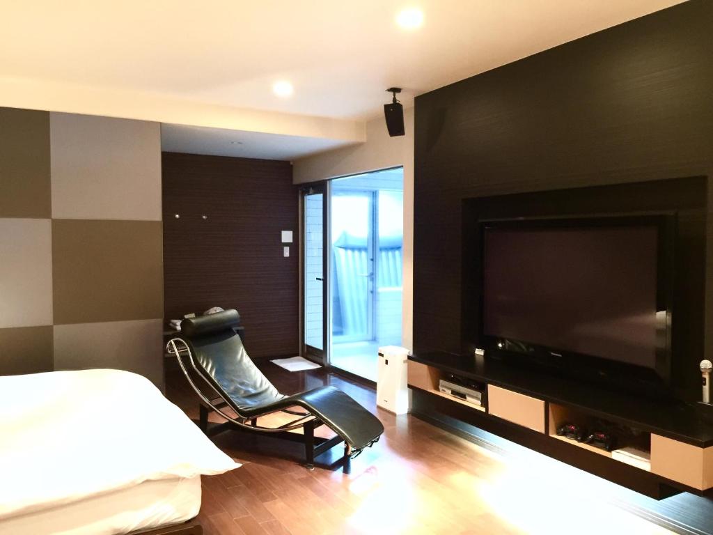 um quarto com uma televisão, uma cama e uma cadeira em LUXe em Higashihiroshima