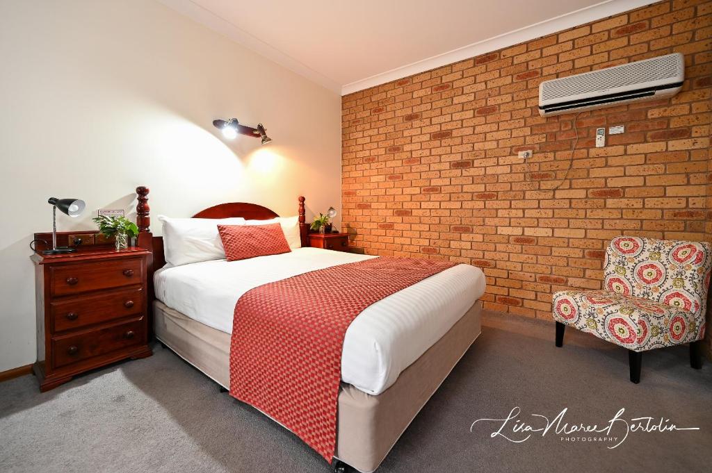 a hotel room with a bed, chair, lamp and a window at Narrandera Club Motor Inn in Narrandera