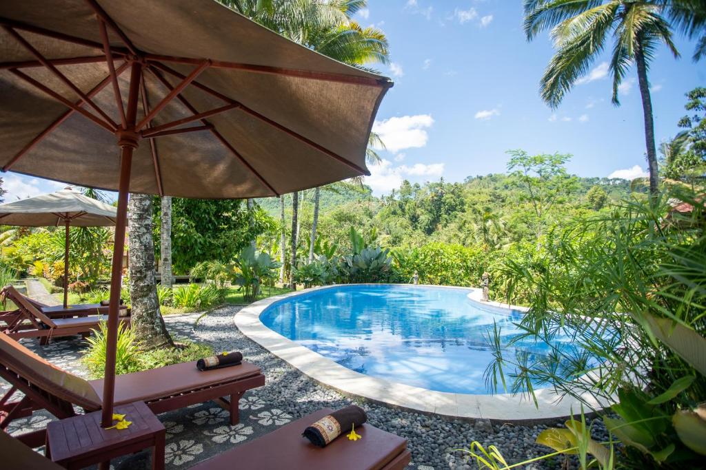 
a patio area with a pool, chairs, and an umbrella at Villa Uma Ayu Sidemen in Sidemen
