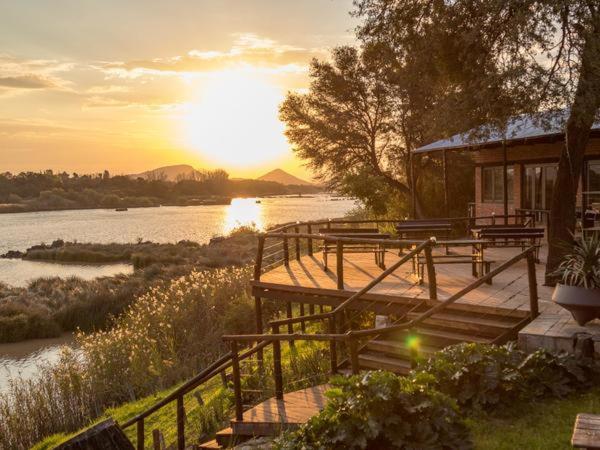 een dok met banken en een huis aan een rivier bij Waschbank River Lodge in Gariepdam