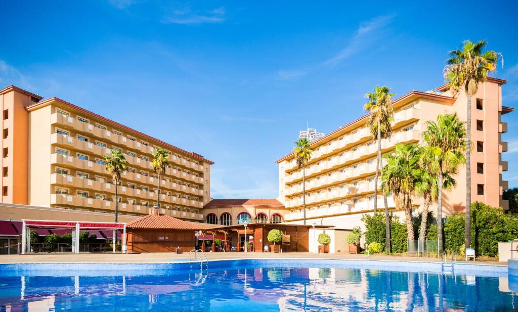 una piscina frente a un hotel con palmeras en Ohtels La Hacienda, en La Pineda