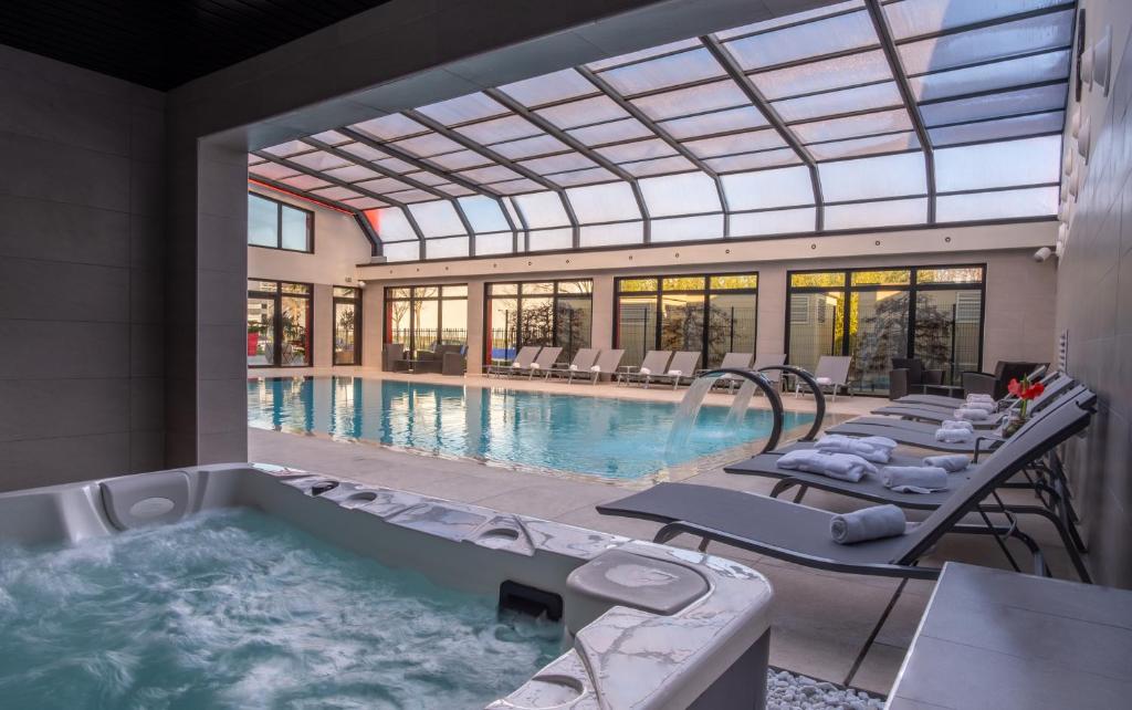 uma grande piscina com uma banheira de hidromassagem numa casa em Kyriad Prestige Lyon Est - Saint Priest Eurexpo Hotel and SPA em Saint-Priest