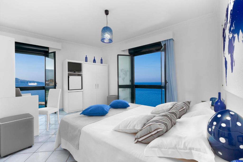 a white bedroom with a large bed with blue pillows at Panorama Palace Hotel in Meta