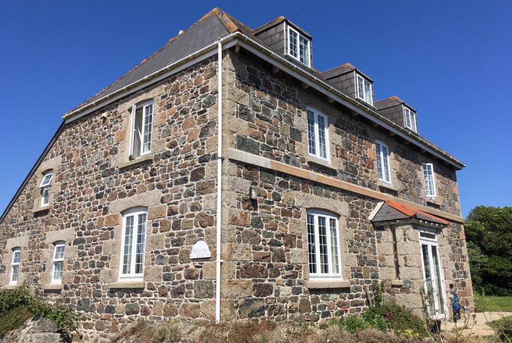 un vieux bâtiment en pierre avec des fenêtres blanches sur une colline dans l'établissement Haelarcher Farmhouse and Helicopter B&B, à Lizard