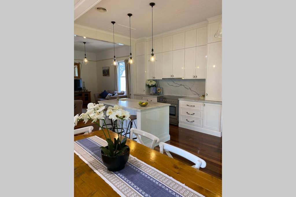 a kitchen with a table and a kitchen with white cabinets at Ashbrooke Cottage in Toowoomba