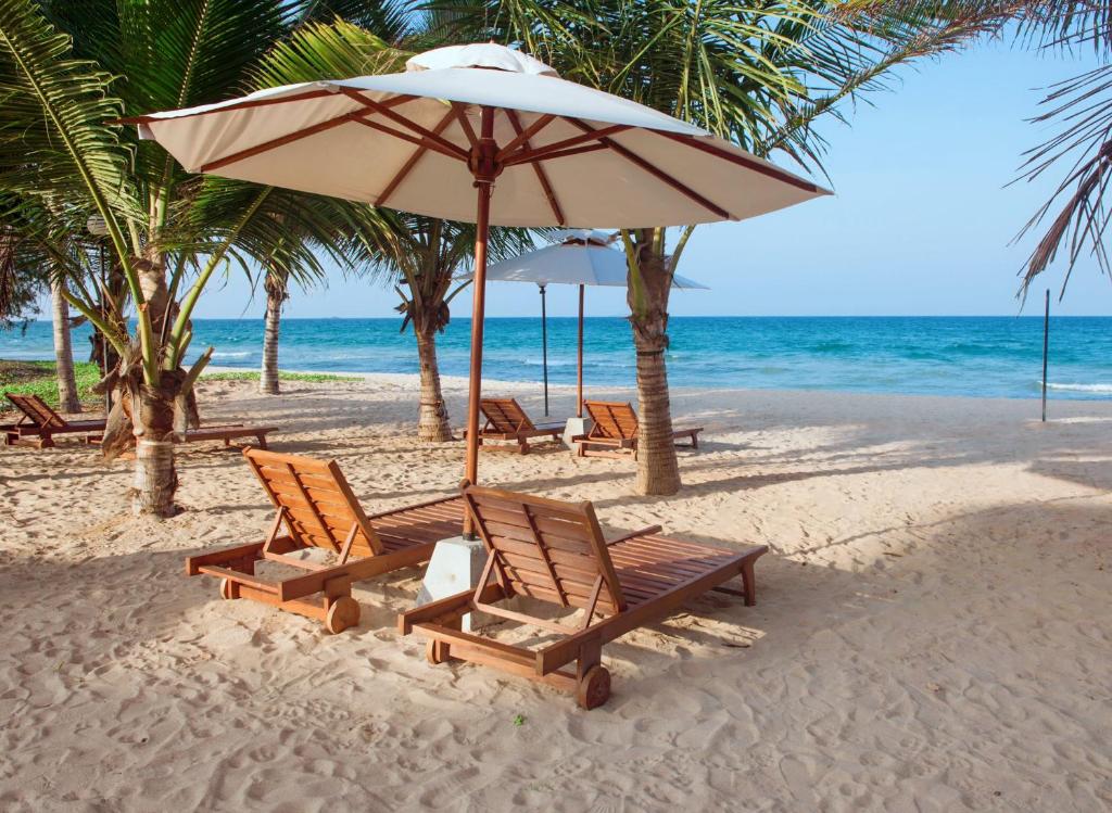 a group of chairs and an umbrella on a beach at Cardamon Hotel Nilaveli in Nilaveli