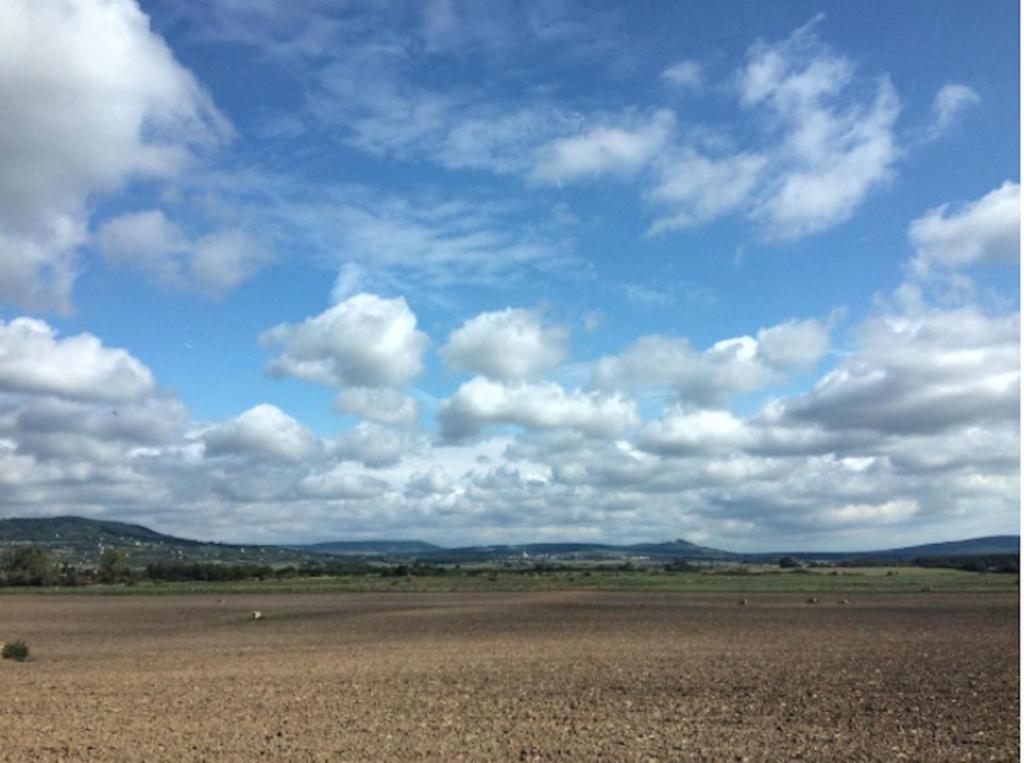 a large open field with a blue sky with clouds at Ablak a hegyre vendégház in Mindszentkálla