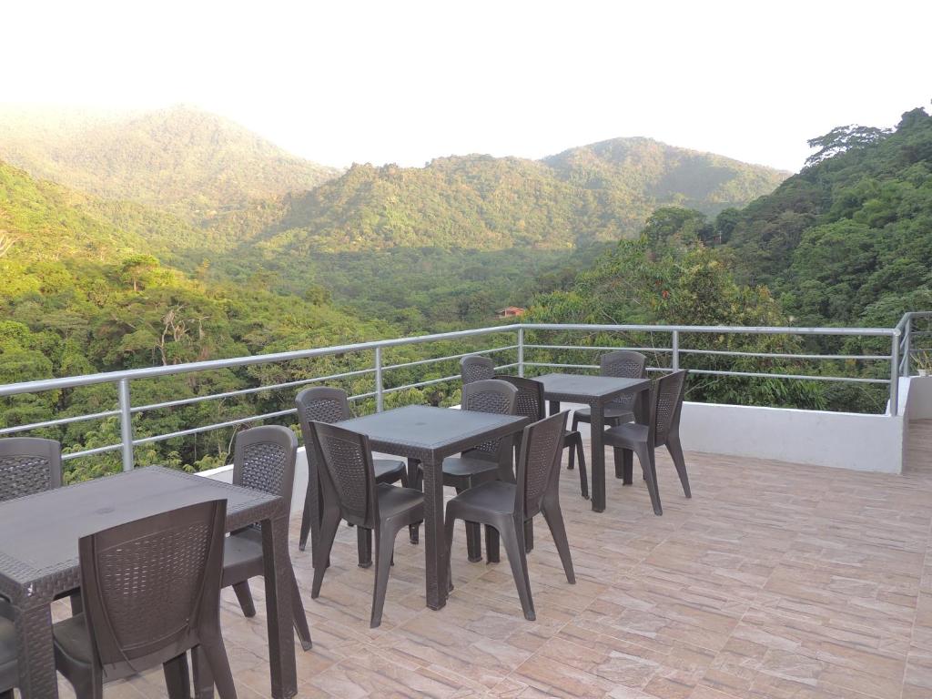 un grupo de mesas y sillas en un balcón con montañas en Hostal Alto de la Montaña, en Minca