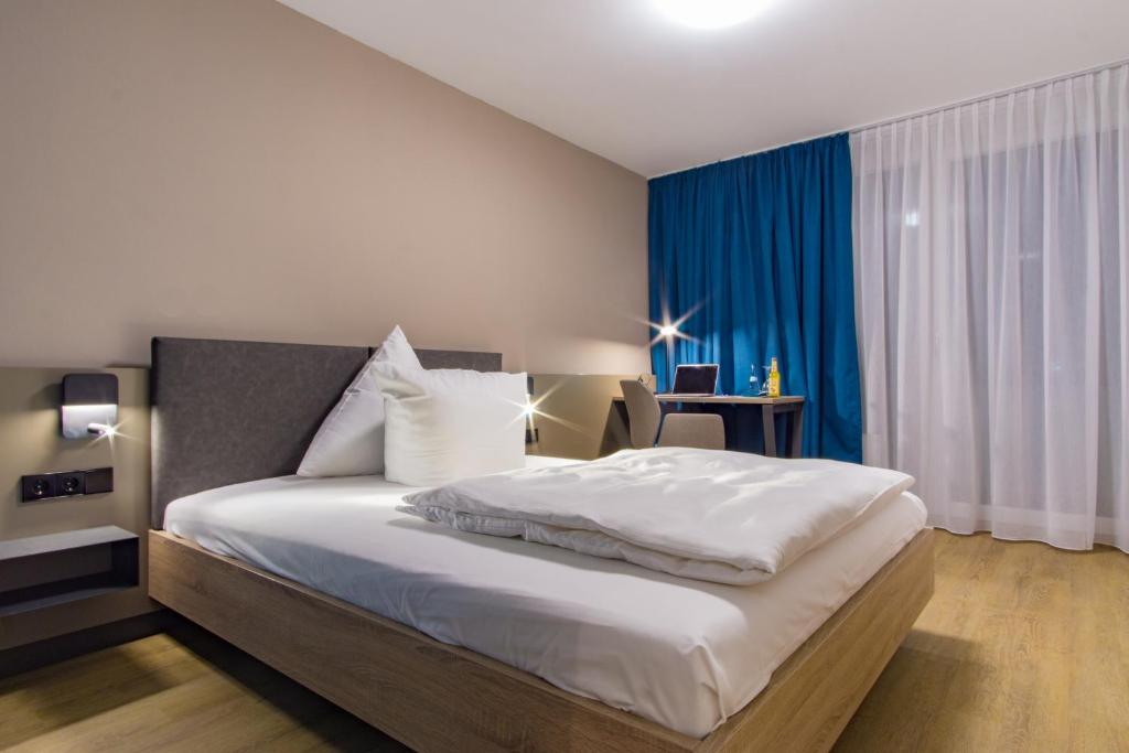 a bedroom with a large white bed with blue curtains at Hotel Berlin in Sindelfingen