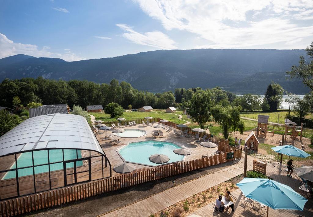 un complejo con piscina y montañas de fondo en Huttopia Lac d'Aiguebelette, en Saint-Alban-de-Montbel