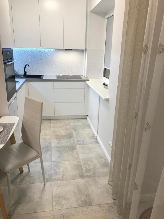 a kitchen with white cabinets and a table and a chair at Central Boulevard Apartment in Šiauliai
