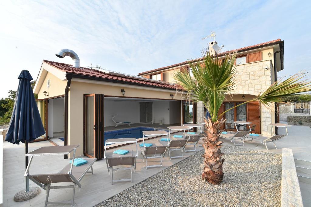 a patio with chairs and a palm tree in front of a house at Villa Muskatel KRK -with heated covered pool in Krk