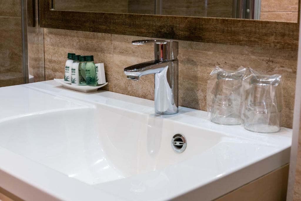 a white bathroom sink with a faucet and glasses at Bükkös Hotel & Spa in Szentendre