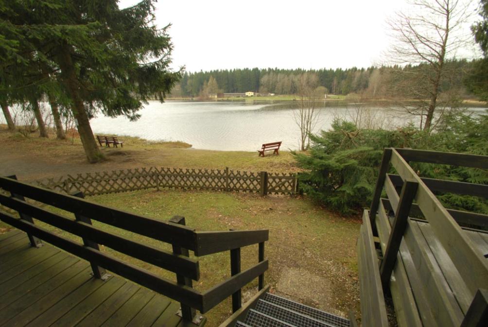 a wooden deck with a bench next to a lake at Holiday park- Nurdach in Clausthal